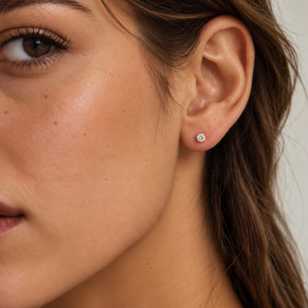A close-up of a woman's ear wearing a small round stud earring in 14k white gold