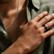 Person wearing a silver necklace and black ring on a green shirt.