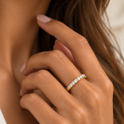 A close-up shot of a woman's hand wearing a 10K yellow gold half-eternity ring set with small round diamonds.