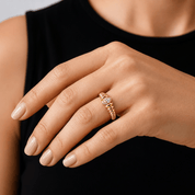 A close-up of a hand wearing a gold ring with small, clear gemstones, against a black sleeveless top.